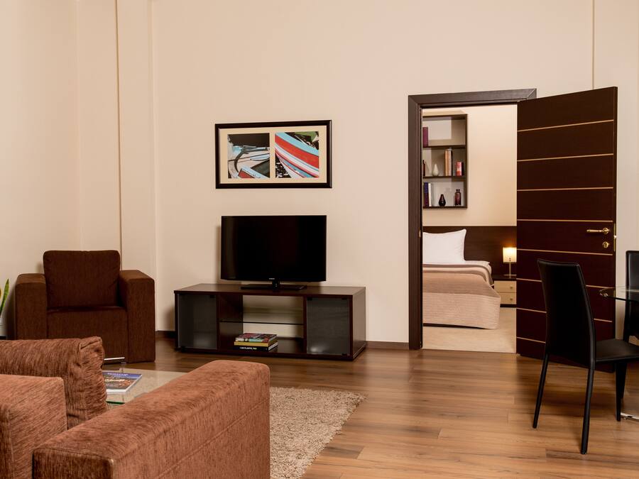 A modern living room with a flat-screen TV, brown sofas, a coffee table, and a bookshelf.
