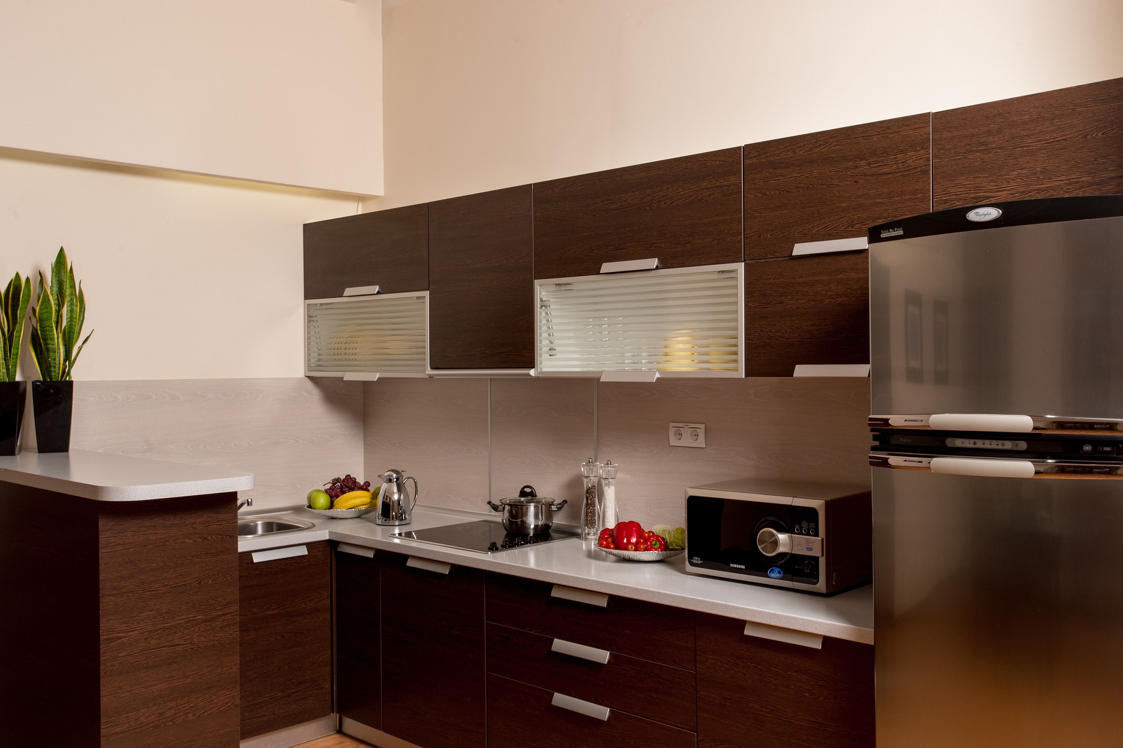 Cocina moderna con refrigerador de acero inoxidable, microondas y horno empotrado. Hay un lavamanos con grifo, una encimera con una planta en maceta y un tazón de frutas.