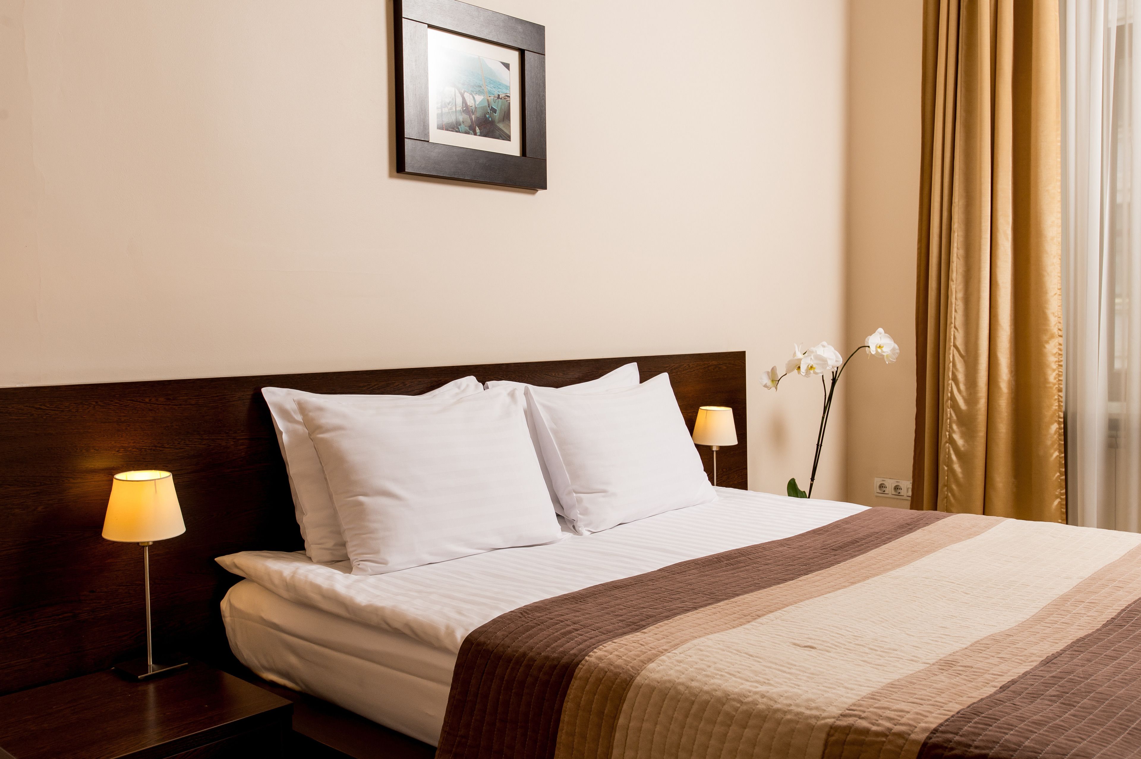 A neatly made bed with white linens and a striped blanket, a bedside lamp, and a framed picture on the wall.