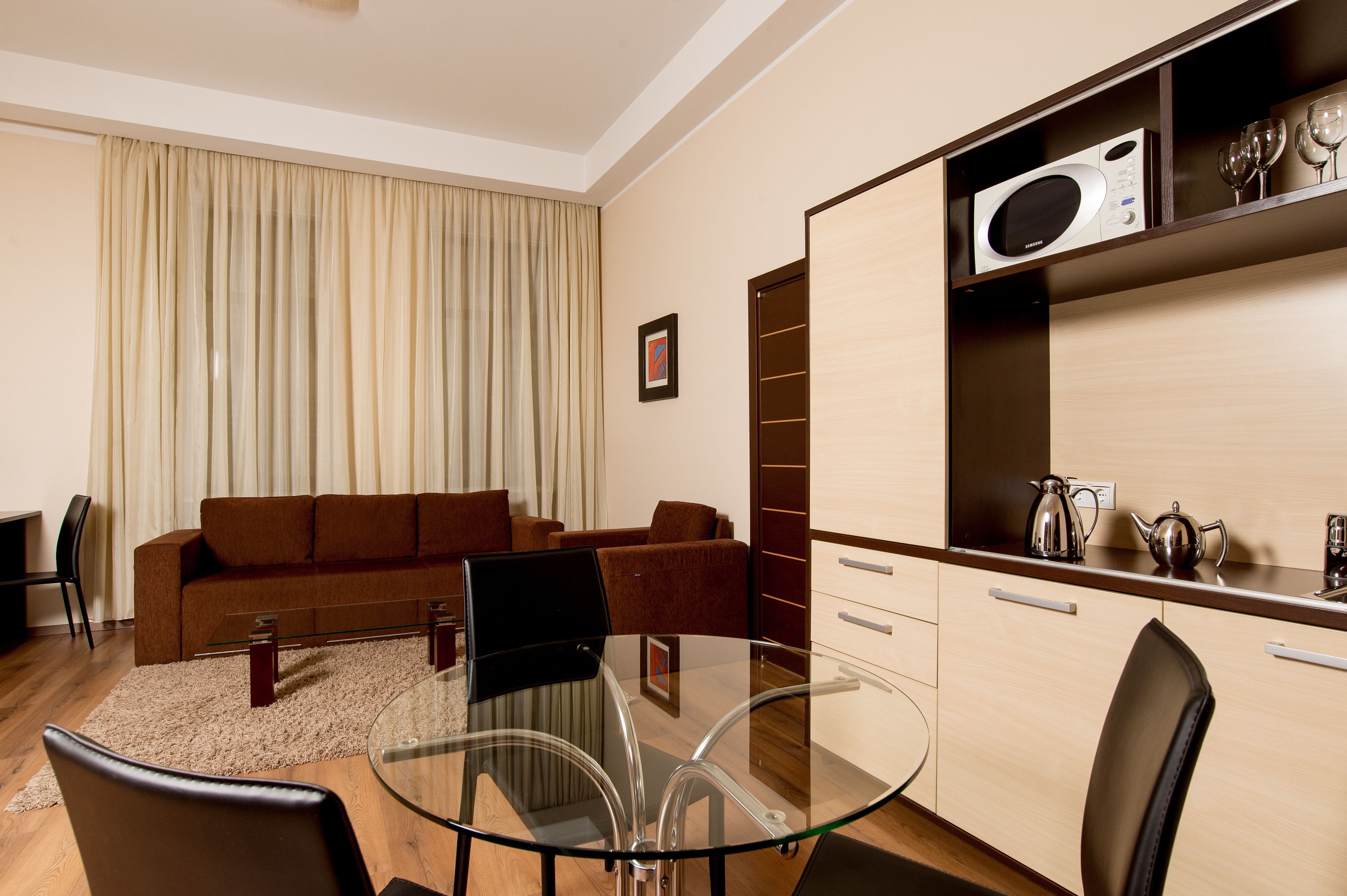 Una sala de estar moderna con una mesa de centro de vidrio, sofá marrón y un comedor con una mesa y sillas de vidrio.