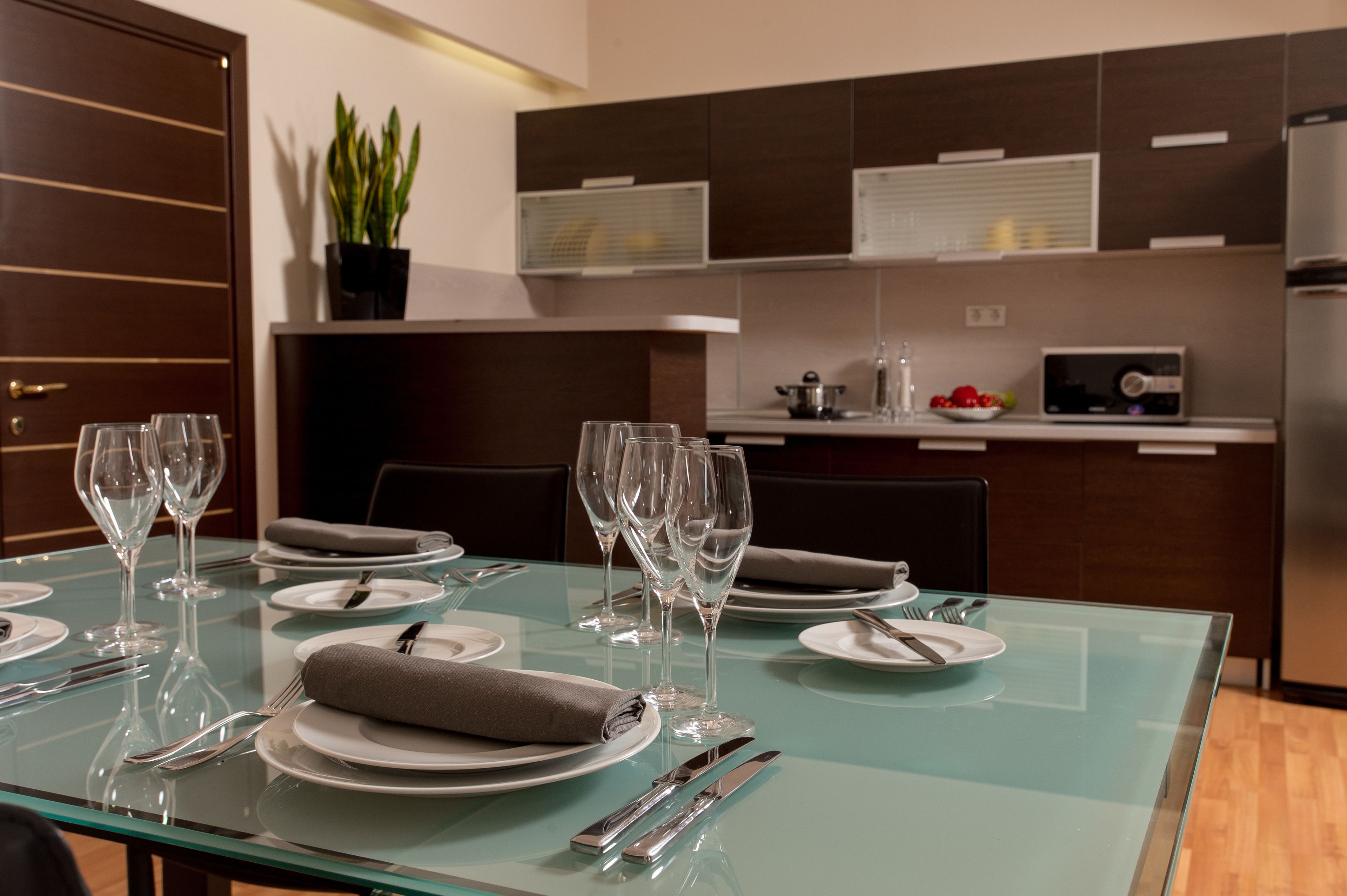 A modern dining area with a glass table set for a meal, including plates, cutlery, and wine glasses.