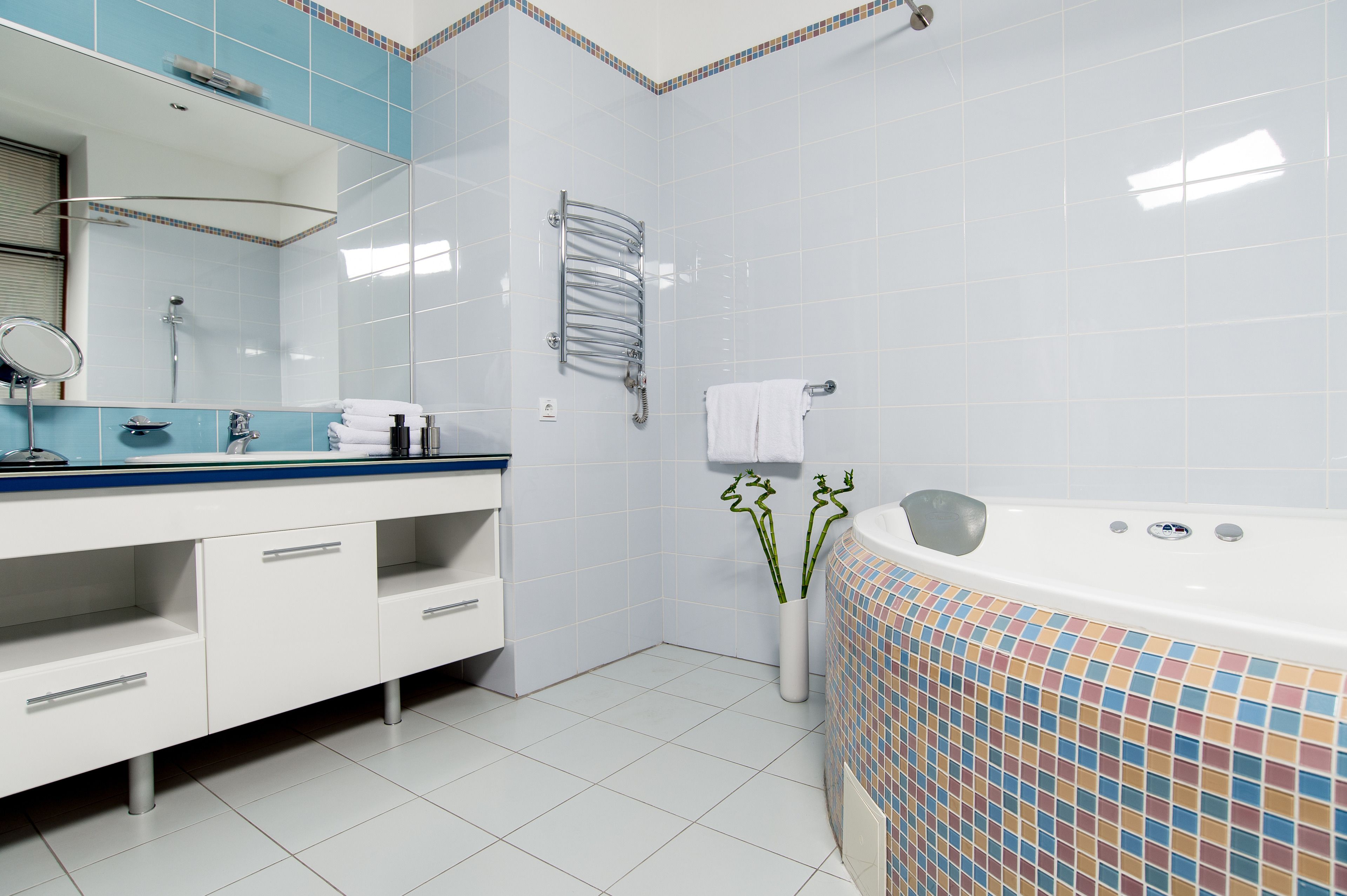 Ein modernes Badezimmer mit einem weißen Waschtisch, einem großen Spiegel, einer Dusche und einer Badewanne mit Mosaikfliesen.