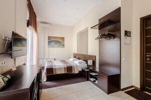 Habitación de hotel con cama, escritorio, televisión, un cuadro y perchero.