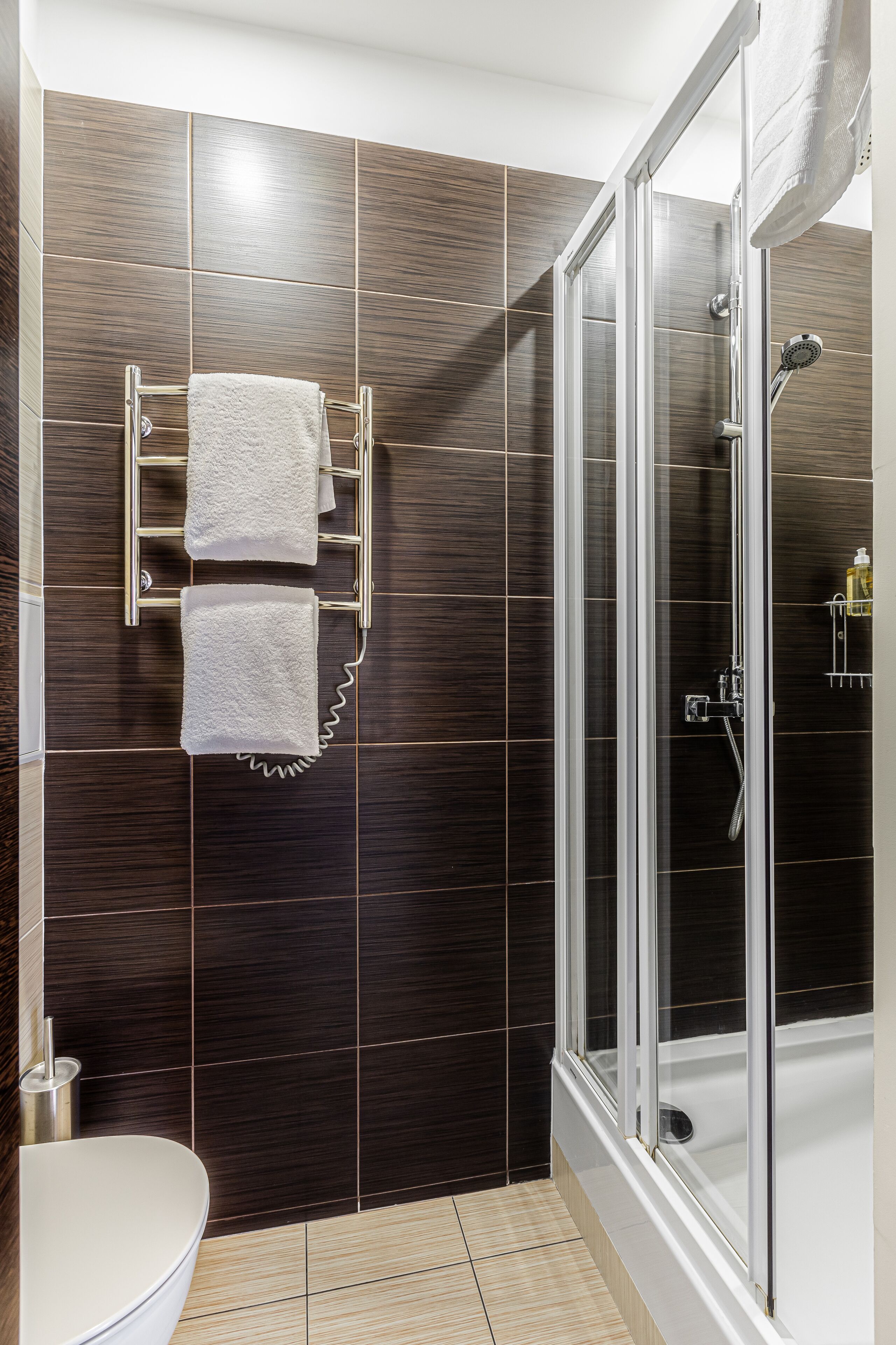 Une salle de bain moderne avec des carreaux de couleur sombre, une douche à parois de verre et des toilettes.