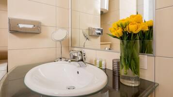 A bathroom with a glass sink, a mirror, and a vase with yellow flowers.