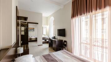 A hotel room with a bed, a desk, a chair, a TV, and a bathroom visible through an archway.