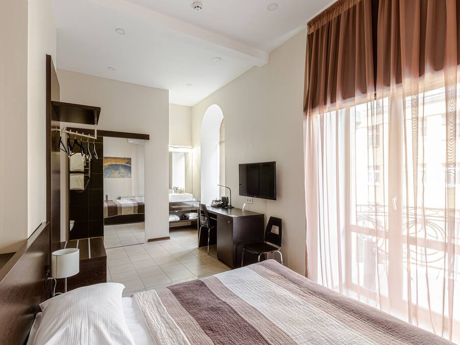 A hotel room with a bed, a desk, a chair, a TV, and a bathroom visible through an archway.