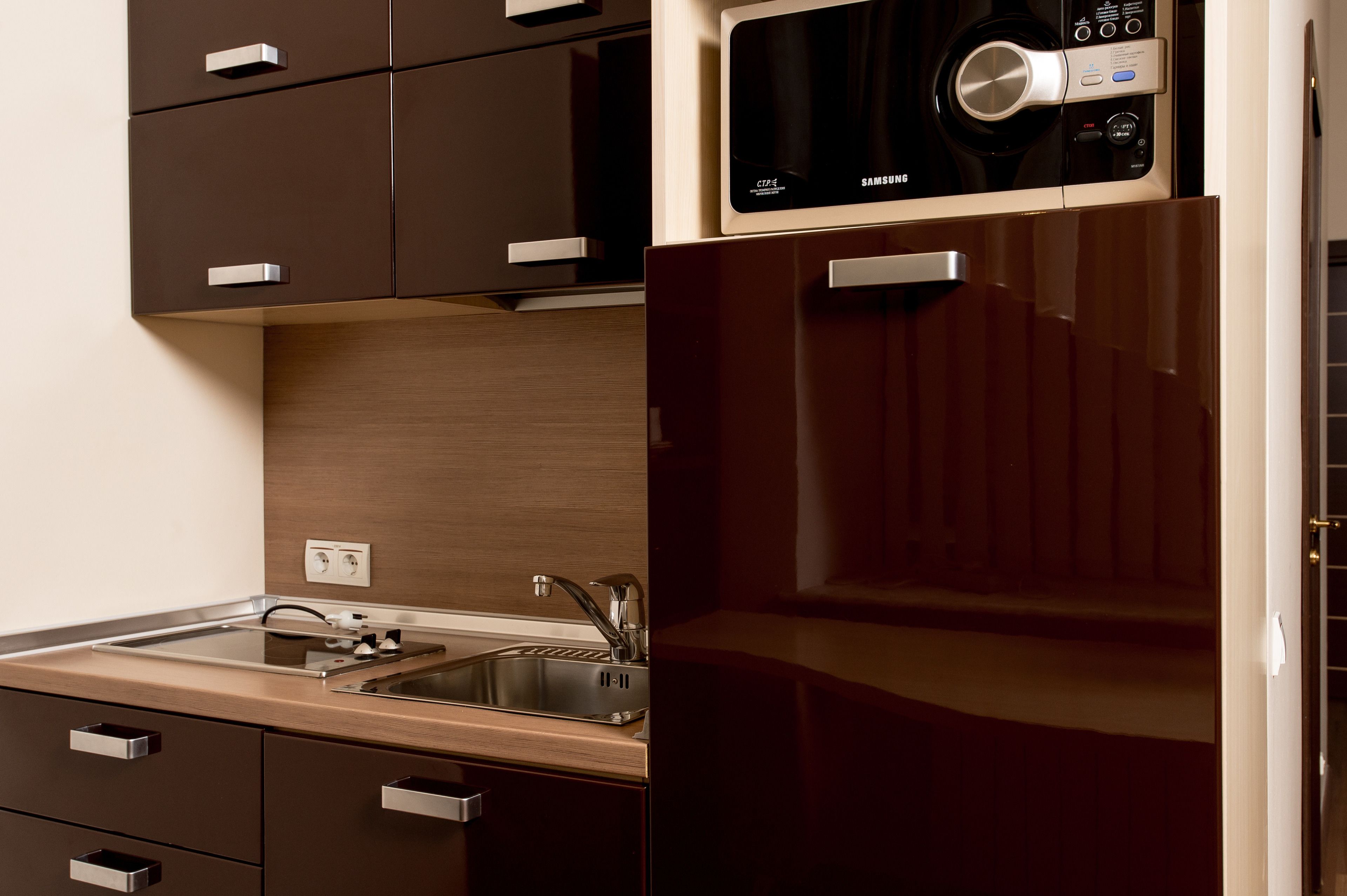 A modern kitchen with a built-in microwave, stainless steel sink, and wooden cabinets.