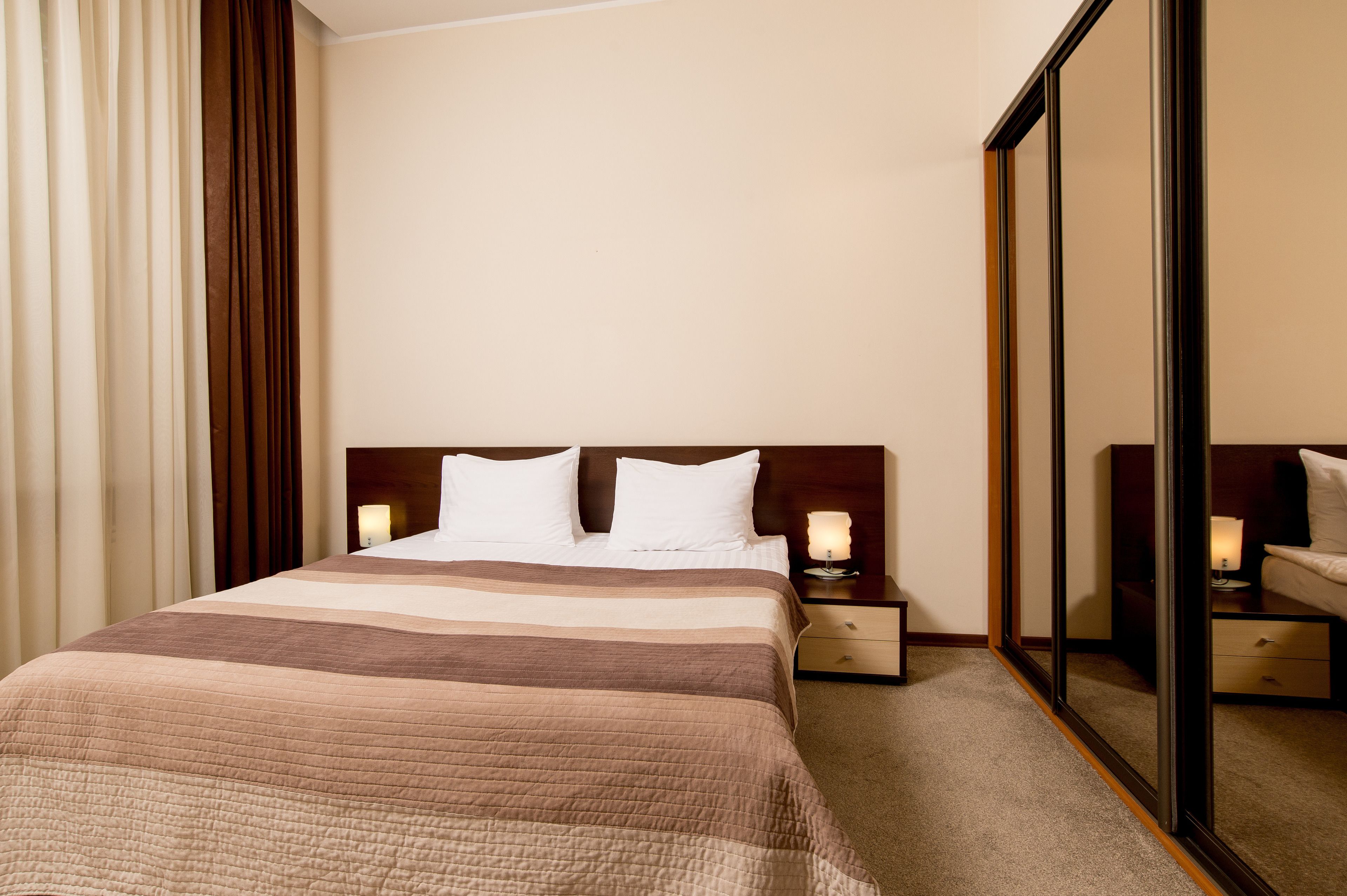 A hotel room with a large bed, two bedside tables with lamps, a mirror, and a wardrobe.