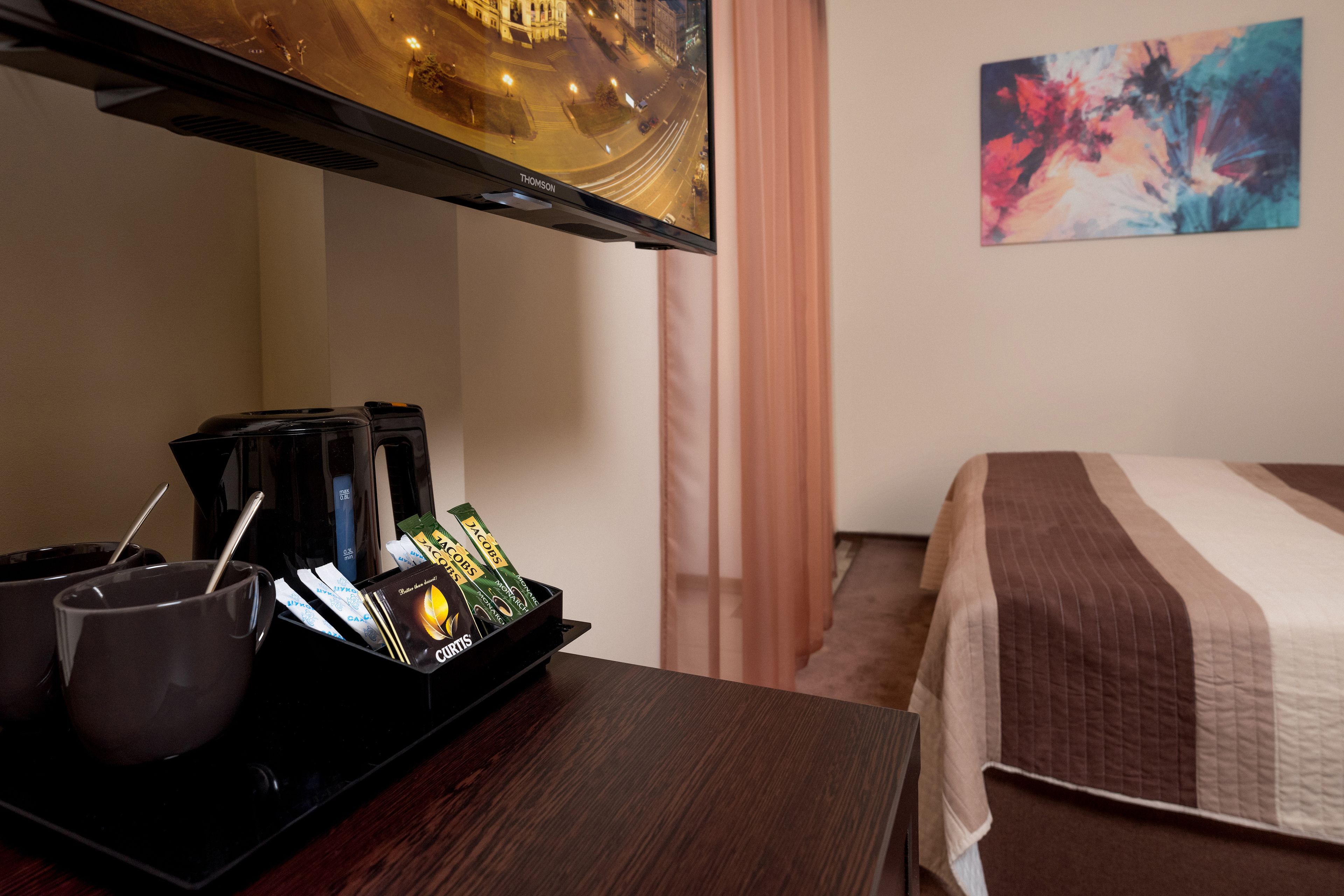A hotel room with a bed, a coffee station, and a TV mounted on the wall.