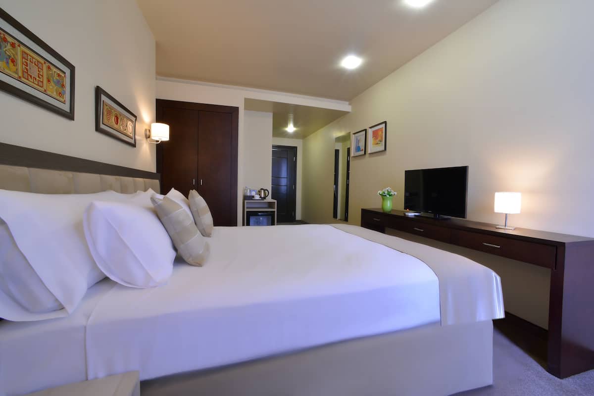 A hotel room with a large bed, a desk with a television, and framed artwork on the walls.