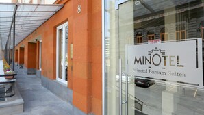 Een hotelentree met een glazen deur, een bordje voor Minotel Barssam Suites, en een overdekte doorgang met oranje muren en een bord met het cijfer '8'.