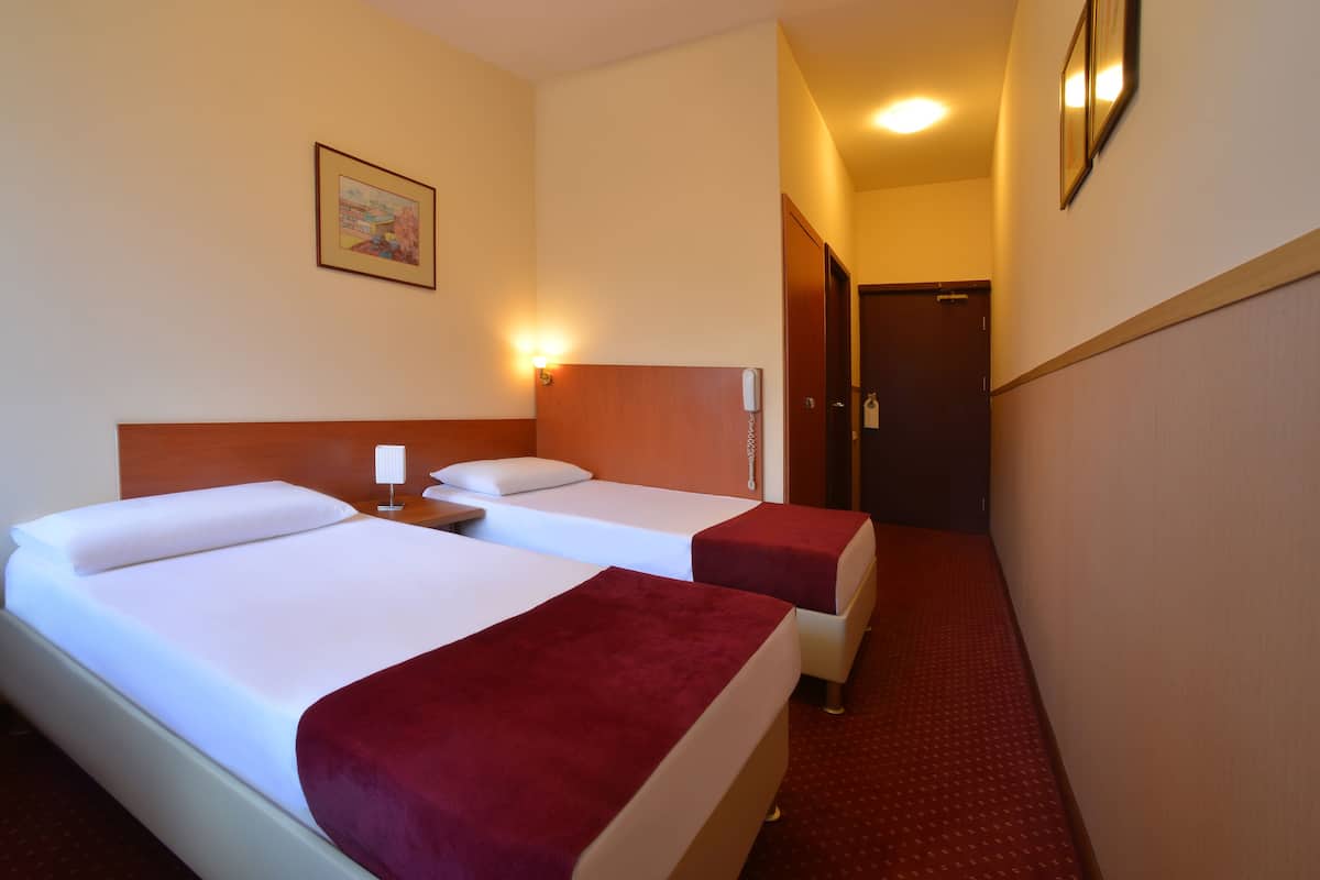 A hotel room with two beds, a nightstand, a wall-mounted phone, and a door leading to another room.