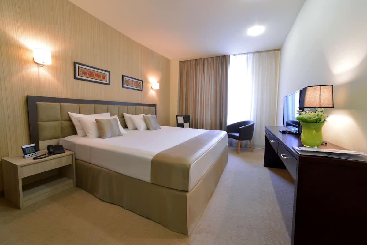 A hotel room with a large bed, bedside tables, a desk, a chair, and a TV.