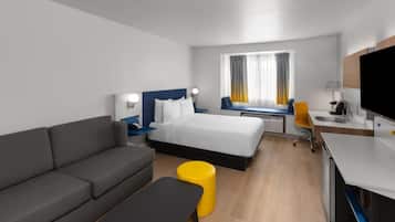 A modern hotel room with a bed, a sofa, a desk, a chair, and a TV.