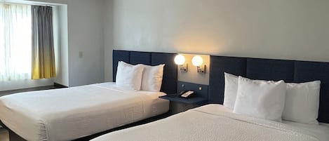 Una camera d'albergo con due letti, un comodino e una finestra con tende.