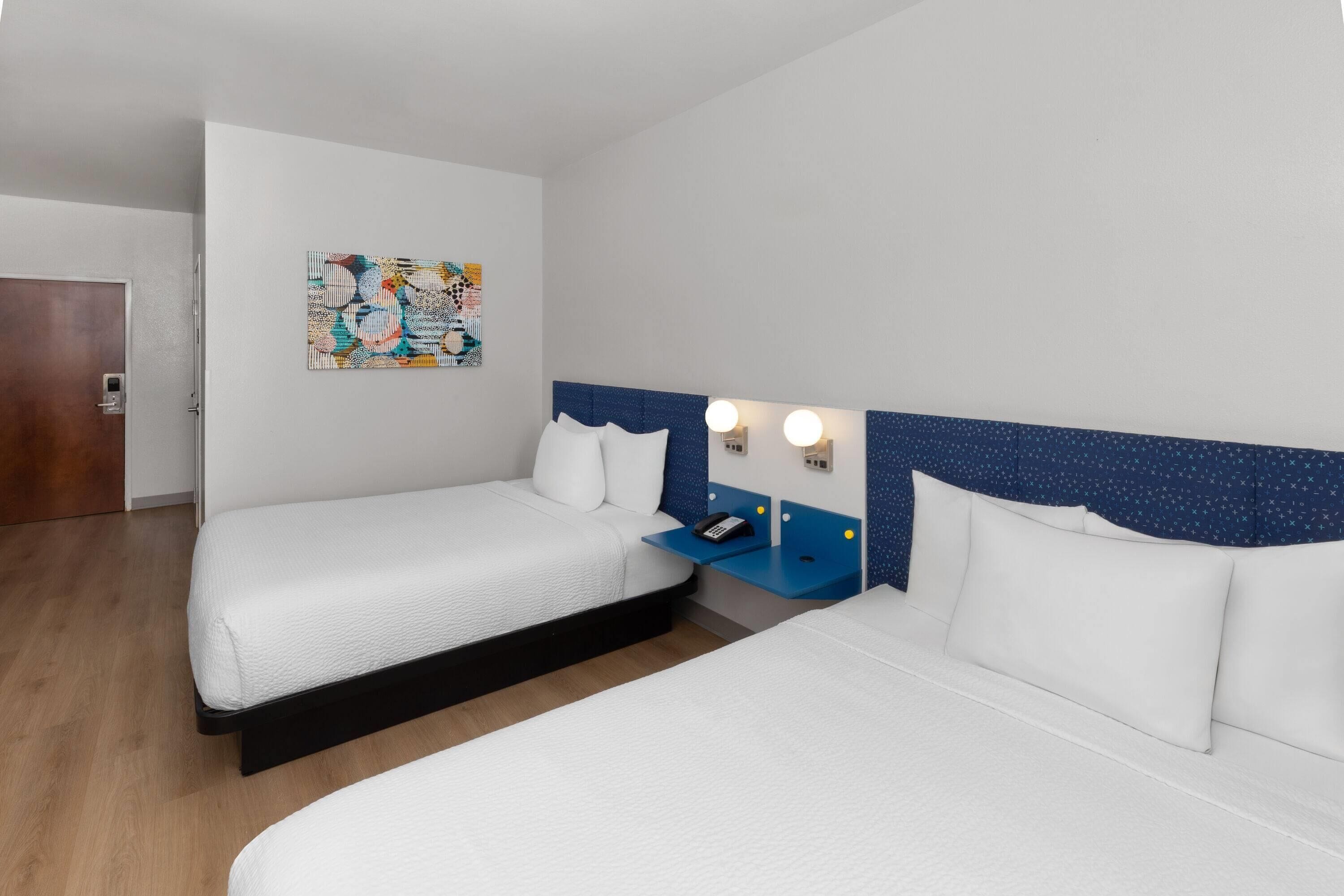 A hotel room with two beds, a nightstand with a phone, and a wall-mounted light fixture.