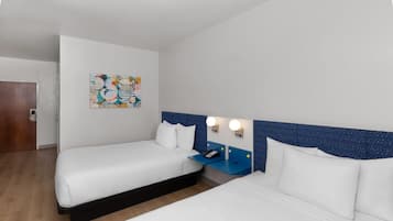A hotel room with two beds, a nightstand with a phone, and a wall-mounted light fixture.