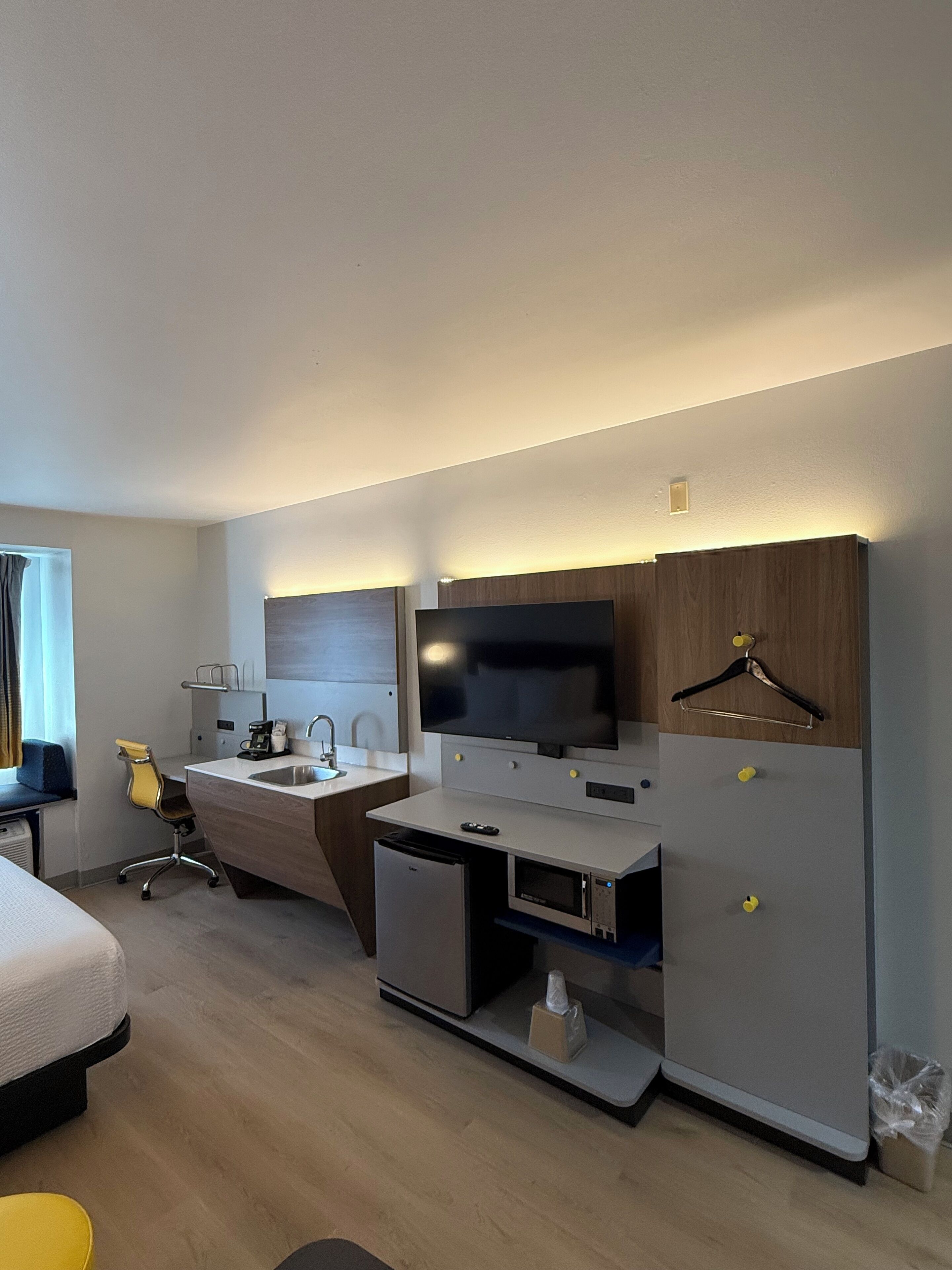 Een moderne hotelkamer met een bed, een bureau met een flatscreen televisie, een minibar, een magnetron en een kleine kitchenette.