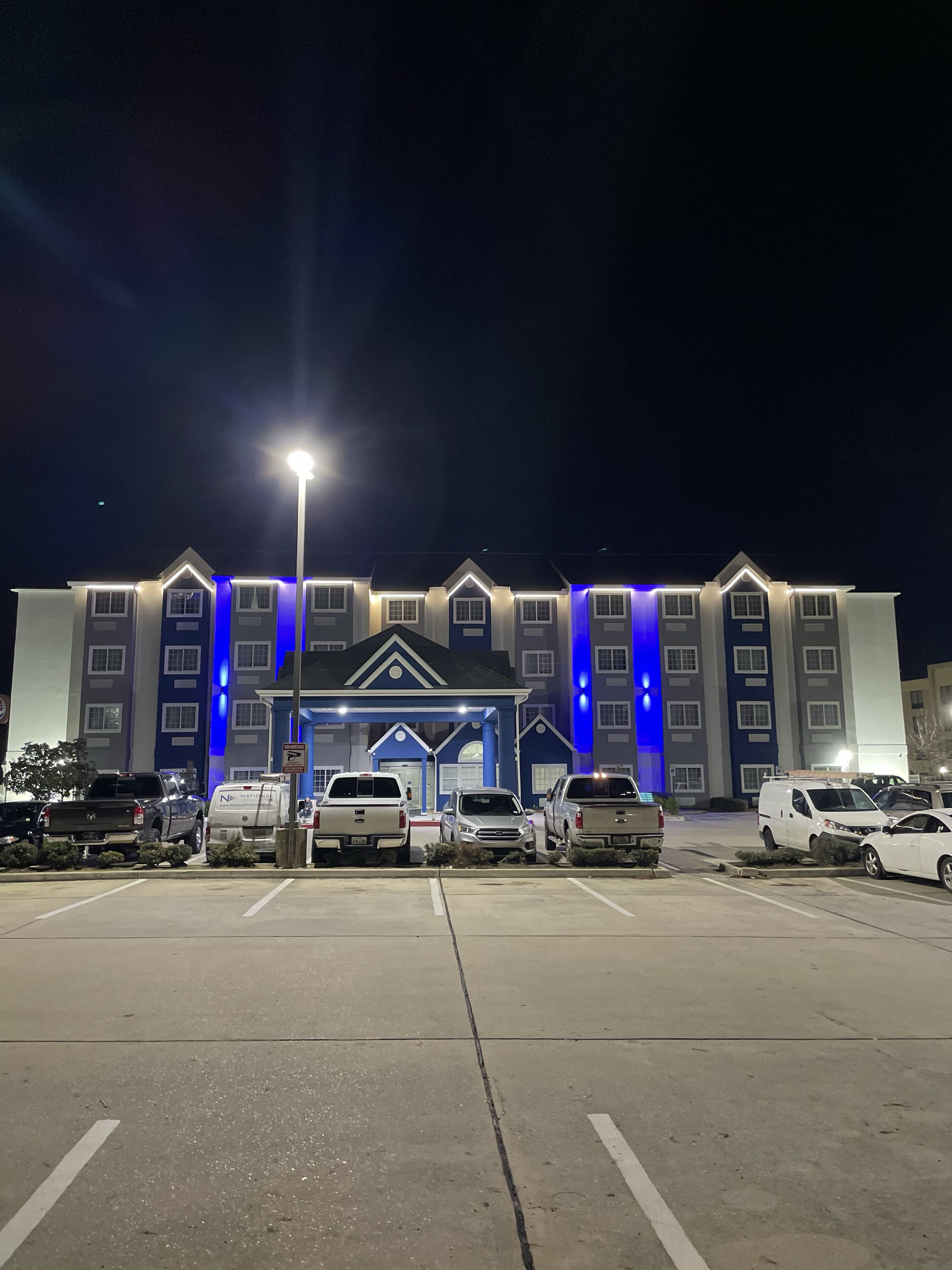 A multi-story hotel with a central entrance, parking lot, and several vehicles parked in front.