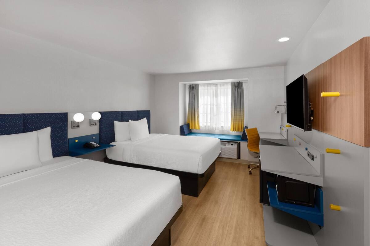A hotel room with two beds, a desk, a chair, a TV, and a window with curtains.