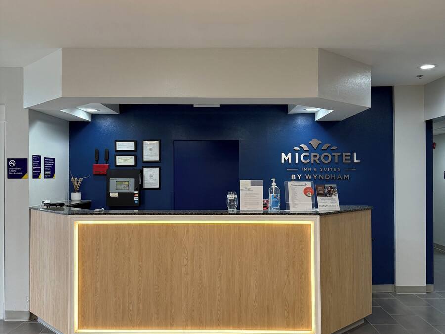 Ein Empfangsschalter mit blauer Wand, einer Holztresen und einer schwarzen Fußmatte mit dem Hotelnamen.