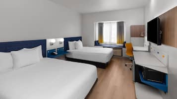 Ein Hotelzimmer mit zwei Betten, einem Schreibtisch, einem Fernseher und einem Fenster mit Vorhängen.