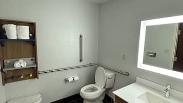 Ein modernes Badezimmer mit einer weißen Toilette, einem Waschbecken und einem Spiegel. Eine Ablagefläche mit Handtüchern und ein kleiner Tritthocker sind vorhanden.