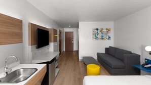 A modern hotel room with a kitchenette, a gray sofa, a bed, and a small yellow ottoman. - Microtel Inn & Suites by Wyndham Baton Rouge Airport (Baton Rouge)