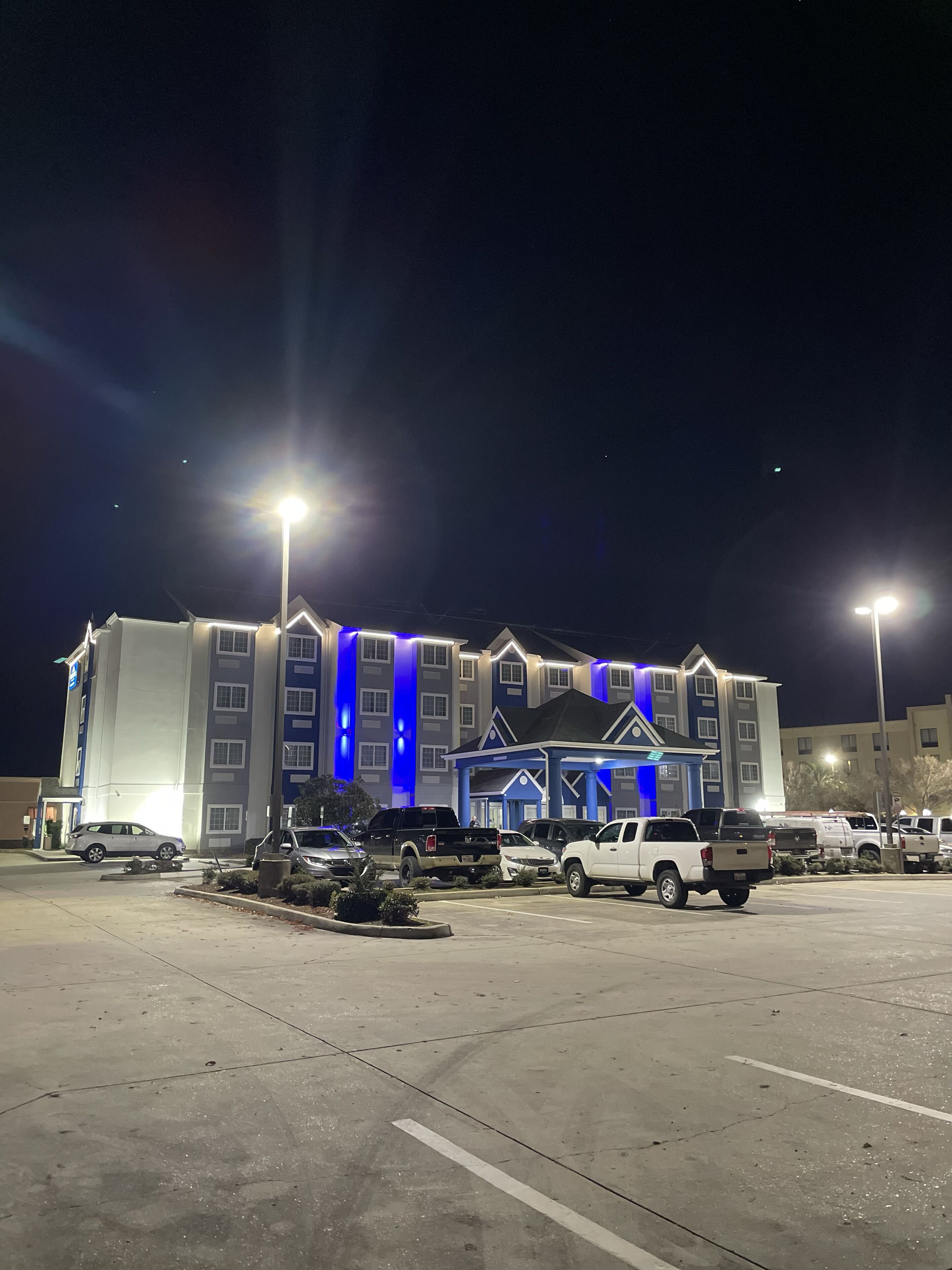 A multi-story hotel with a modern design, featuring a prominent blue accent wall and a parking lot with several vehicles.