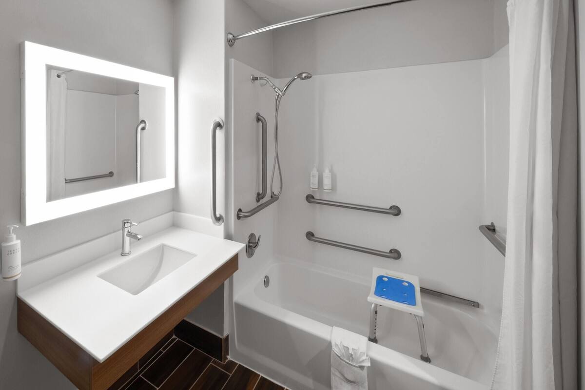 A modern bathroom with a sink, mirror, shower, and grab bars.