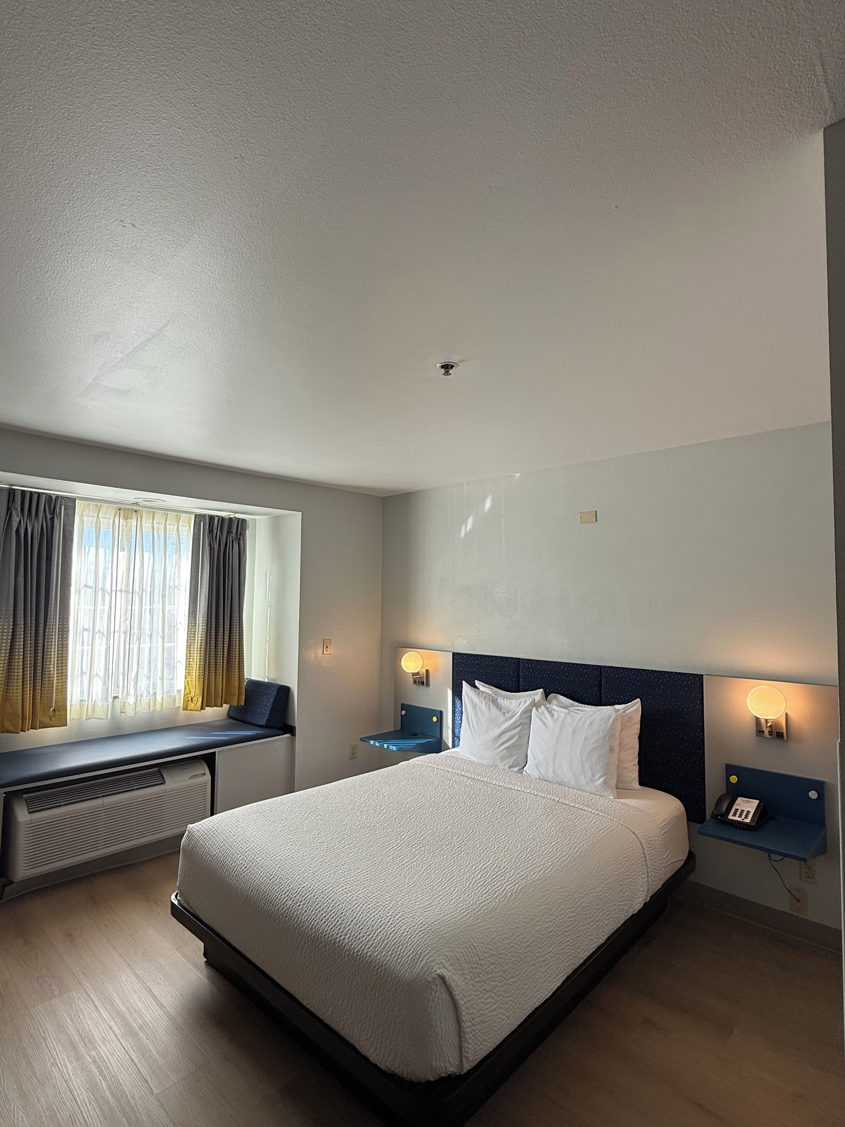 Habitación de hotel con una cama grande, mesitas de noche con lámparas, una ventana con cortinas y un radiador.