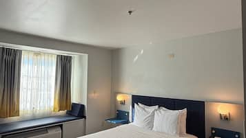 Habitación de hotel con una cama grande, mesitas de noche con lámparas, una ventana con cortinas y un radiador.