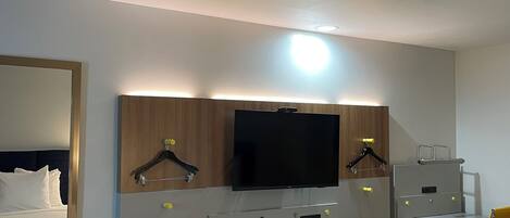 Una camera d'albergo con un letto, una scrivania con un computer, una televisione sopra la scrivania e una sedia.