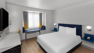 A hotel room with a bed, a desk, a TV, a window with curtains, and a nightstand with a phone.