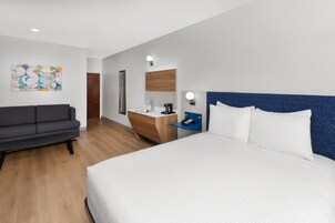 A hotel room with a bed, a sofa, a desk with a mirror, and a wall-mounted phone.
