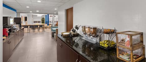 A modern kitchen with a long counter, a coffee station, and a seating area in the background.