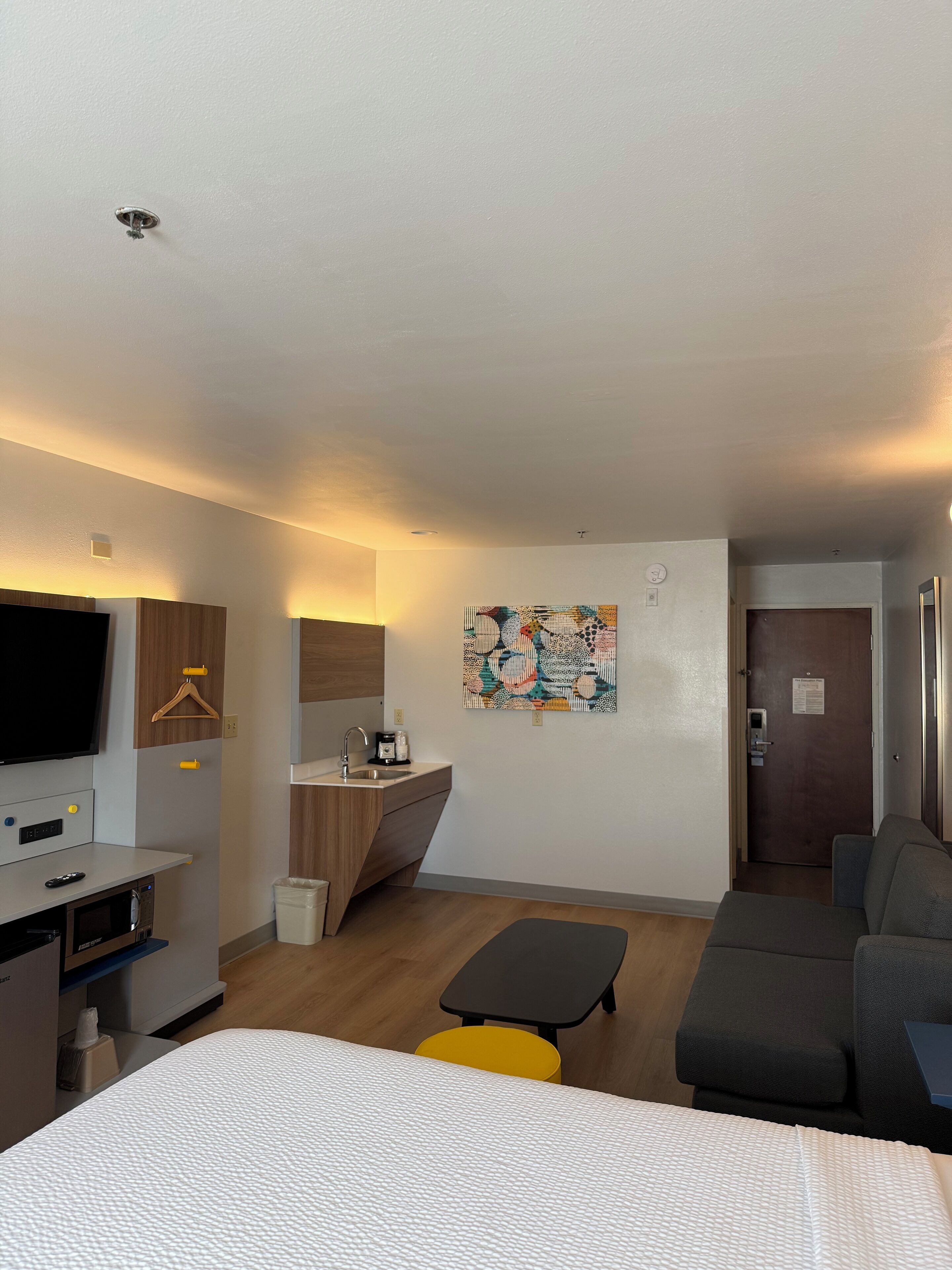 Habitación de hotel moderna con cama, escritorio con lavamanos, televisor y un cuadro en la pared.