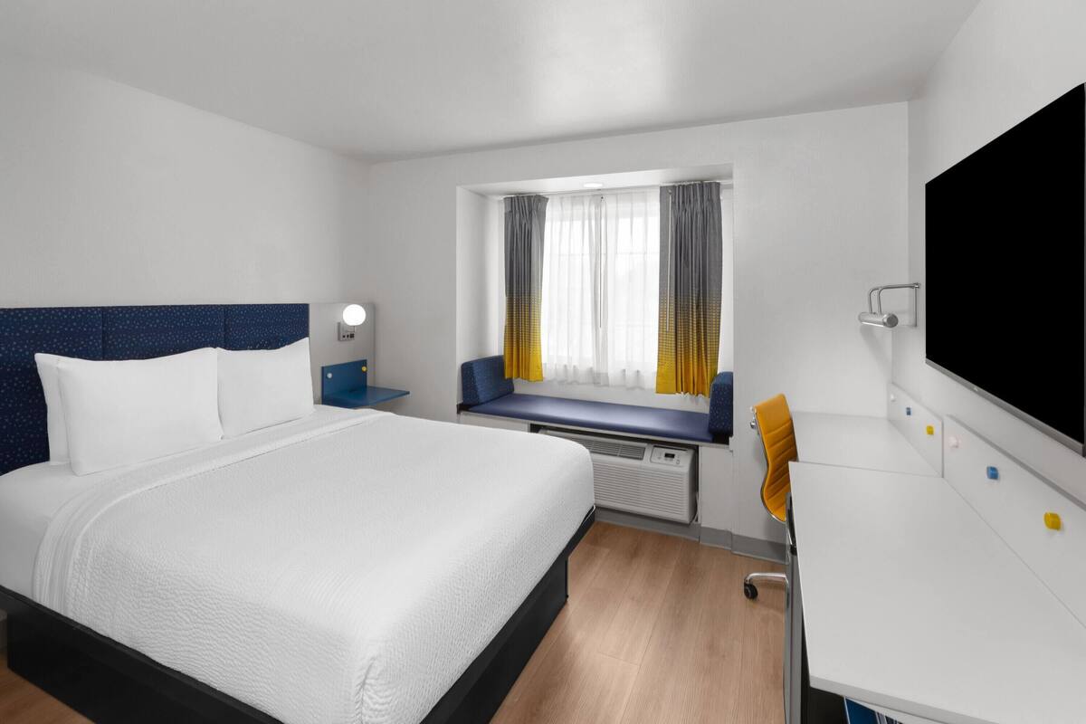 A hotel room with a bed, a desk, a window with curtains, and a TV.