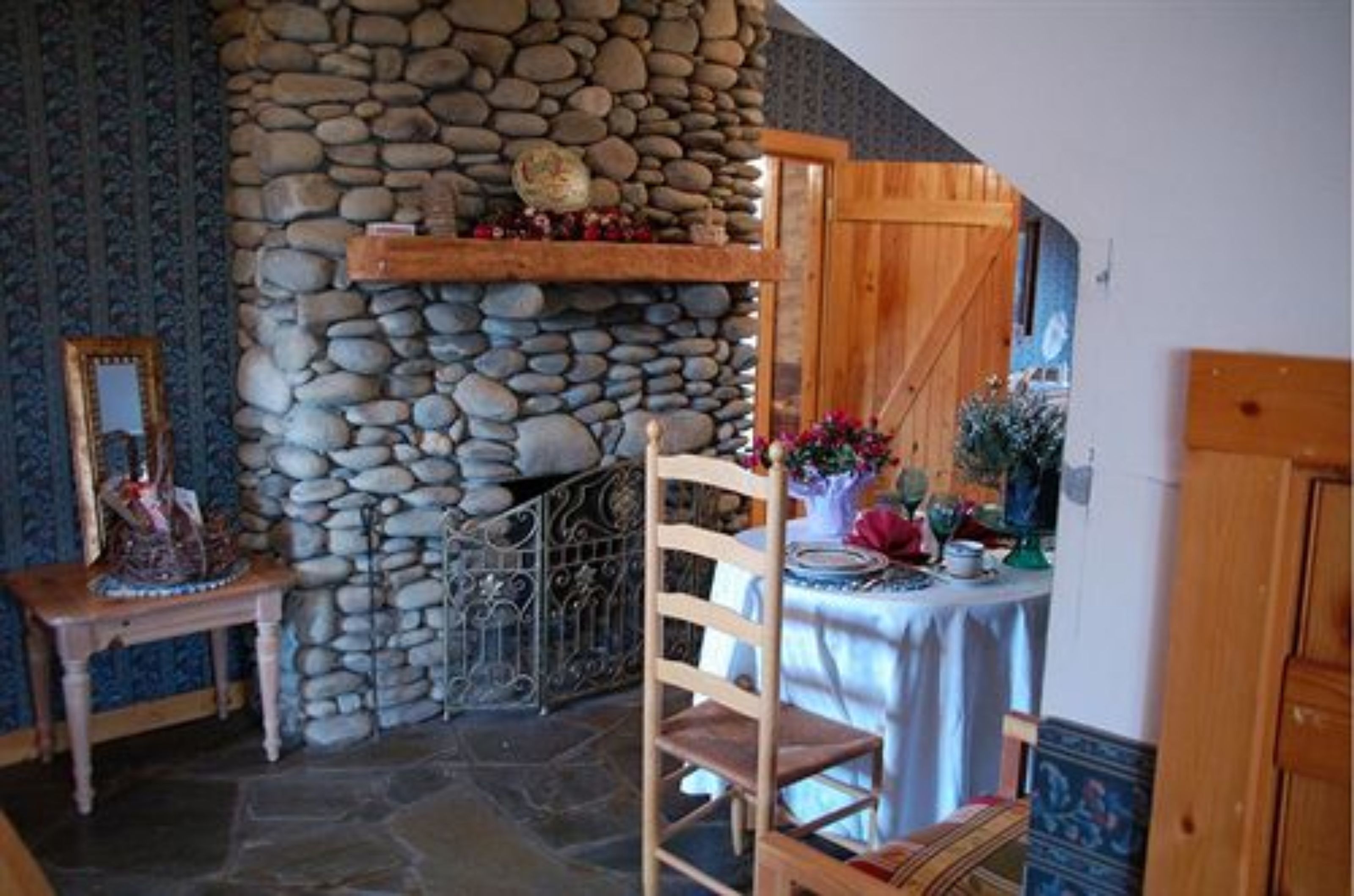 Una habitación con pared de piedra, puerta de madera, una mesa con mantel y una silla.