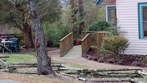 Ein Haus mit einer Holzterrasse, einer kleinen Veranda und einem Garten mit verschiedenen Pflanzen und Blumen.