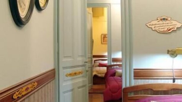 Une chambre d’hôtel avec un plancher en bois, un lit recouvert d’une couverture rouge, une tête de lit en bois et une porte dotée d’un cadre blanc.