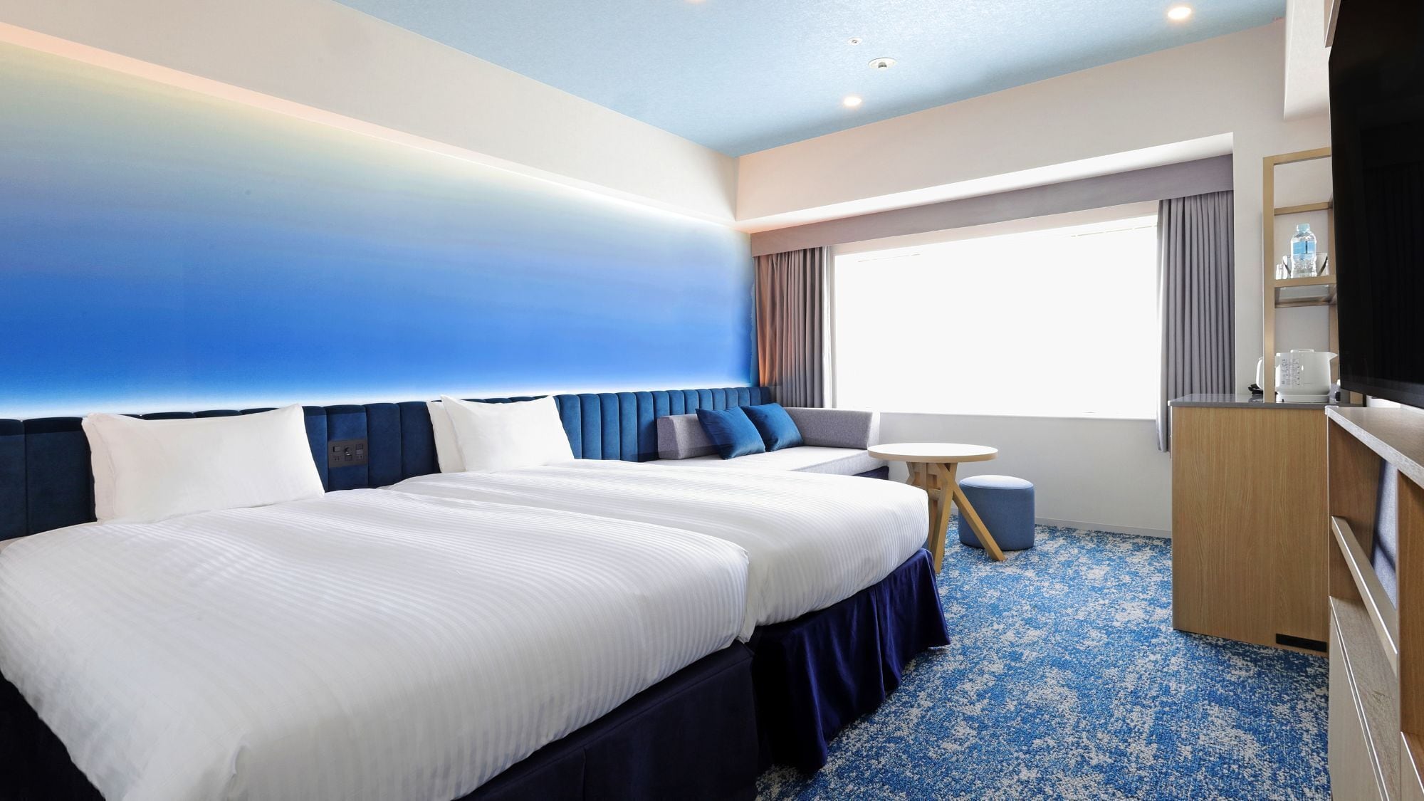 Ein Hotelzimmer mit einem großen Bett, einem kleinen Tisch, einem Fernseher und einem Fenster mit Vorhängen.
