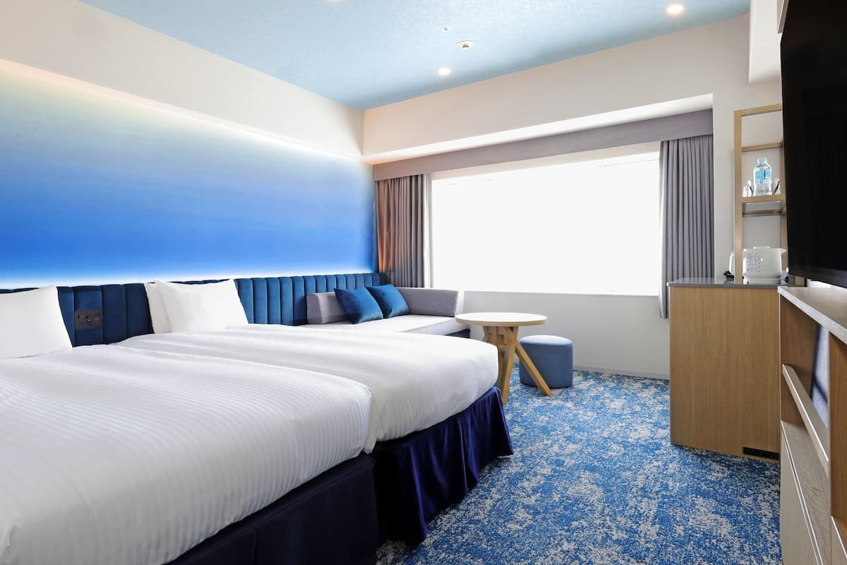 A hotel room with a large bed, a small table, a TV, and a window with curtains.