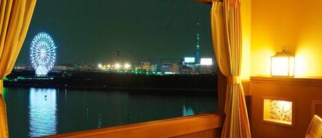 A room with a large window overlooking a cityscape at night, featuring a Ferris wheel and a tall building.