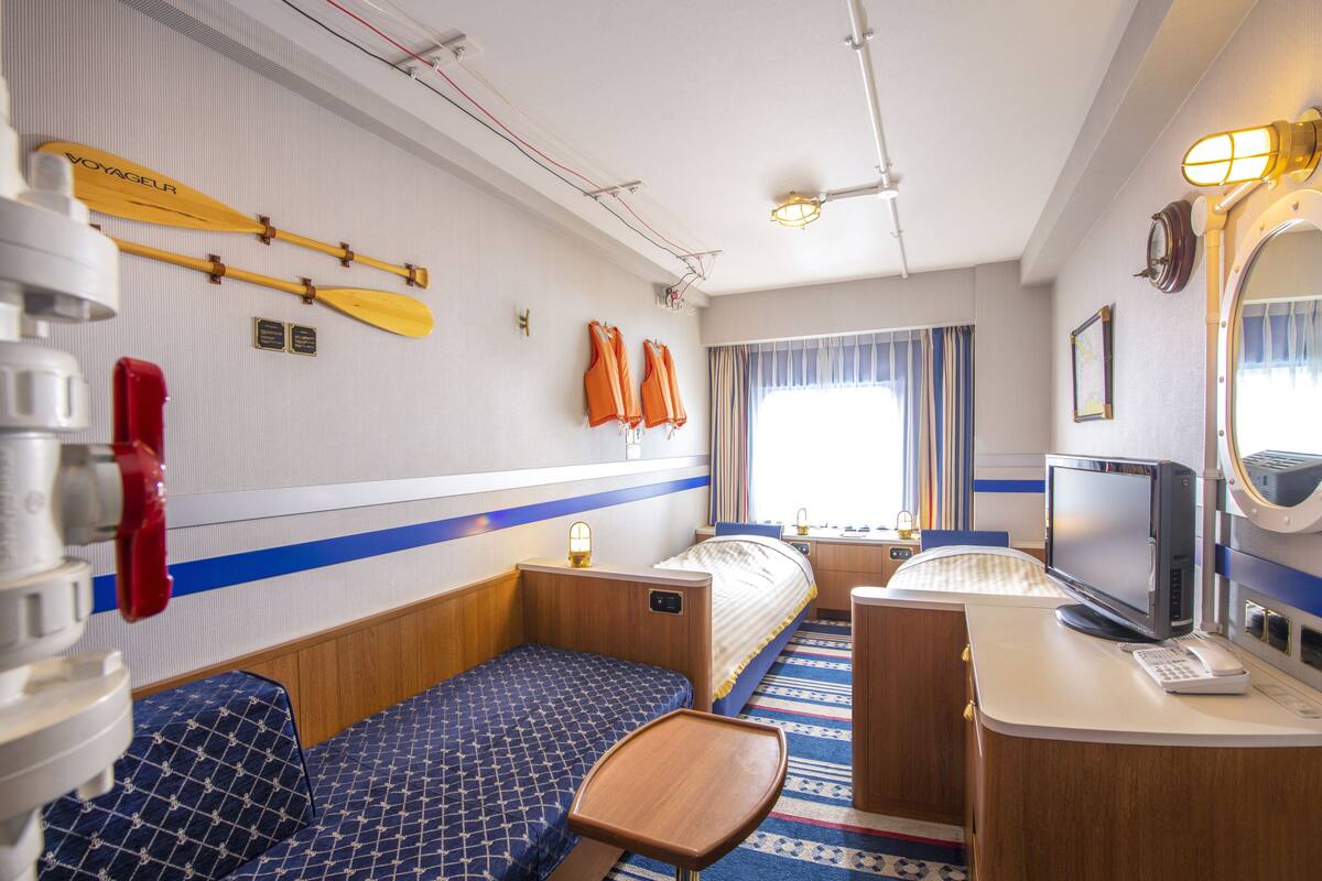 A compact hotel room with a bed, a small seating area, a desk with a computer, and a window with curtains.