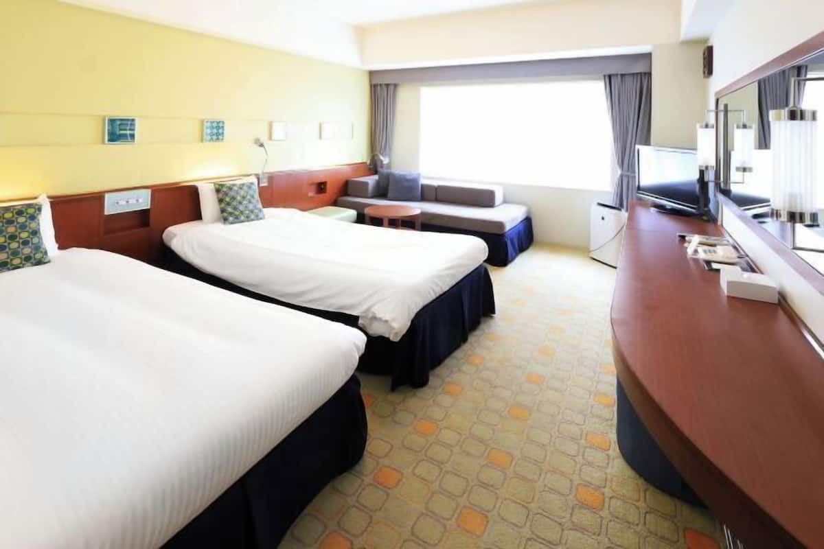 A hotel room with two beds, a sofa, a TV, and a small table.