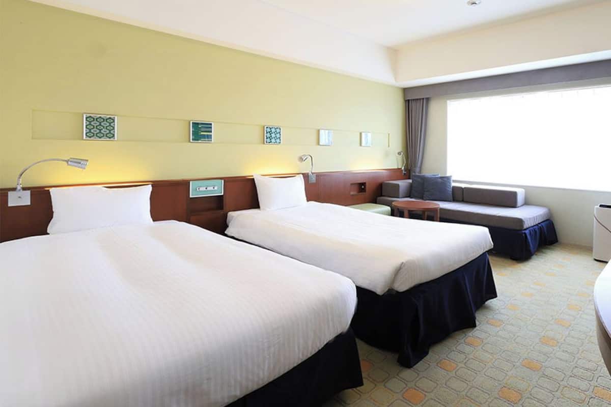 A hotel room with two beds, a desk, a chair, a TV, and a window.