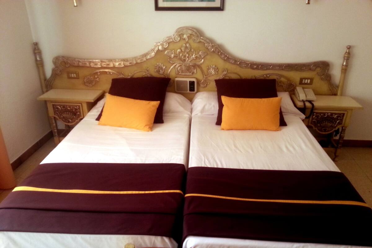 Una cama doble con dos almohadas, una mesita de noche con teléfono y un cabecero decorativo.