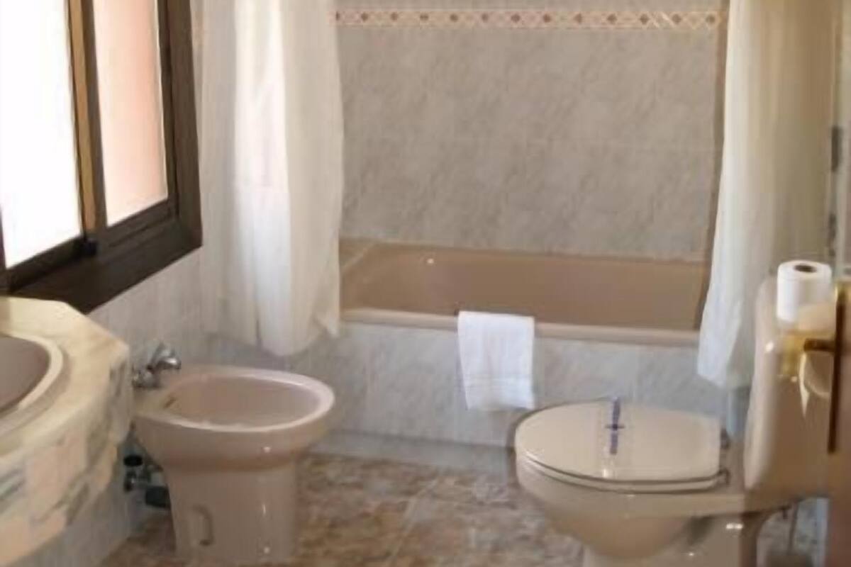 Un baño con bañera, inodoro, bidé y una ventana con cortinas.